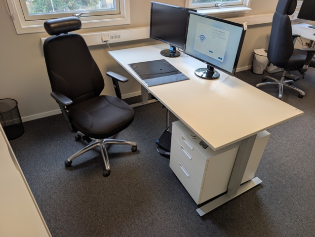 Arbetsplats med elskrivbord, arbetsstol och skåp