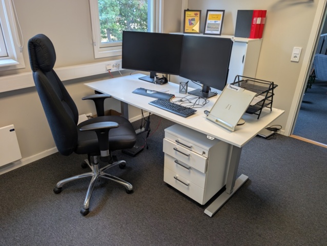 Arbetsplats med elskrivbord, arbetsstol och skåp